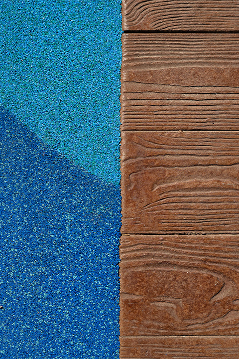 Detail of rubberized play surfacing meeting wood-textured stamped concrete